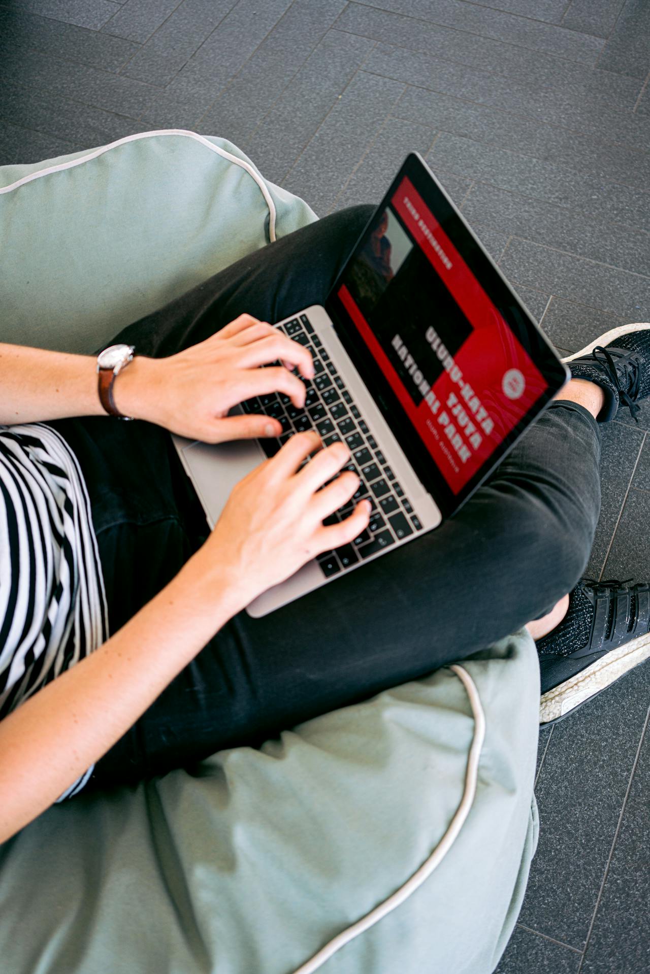 a person sitting on green bean bag, and typing on a laptop